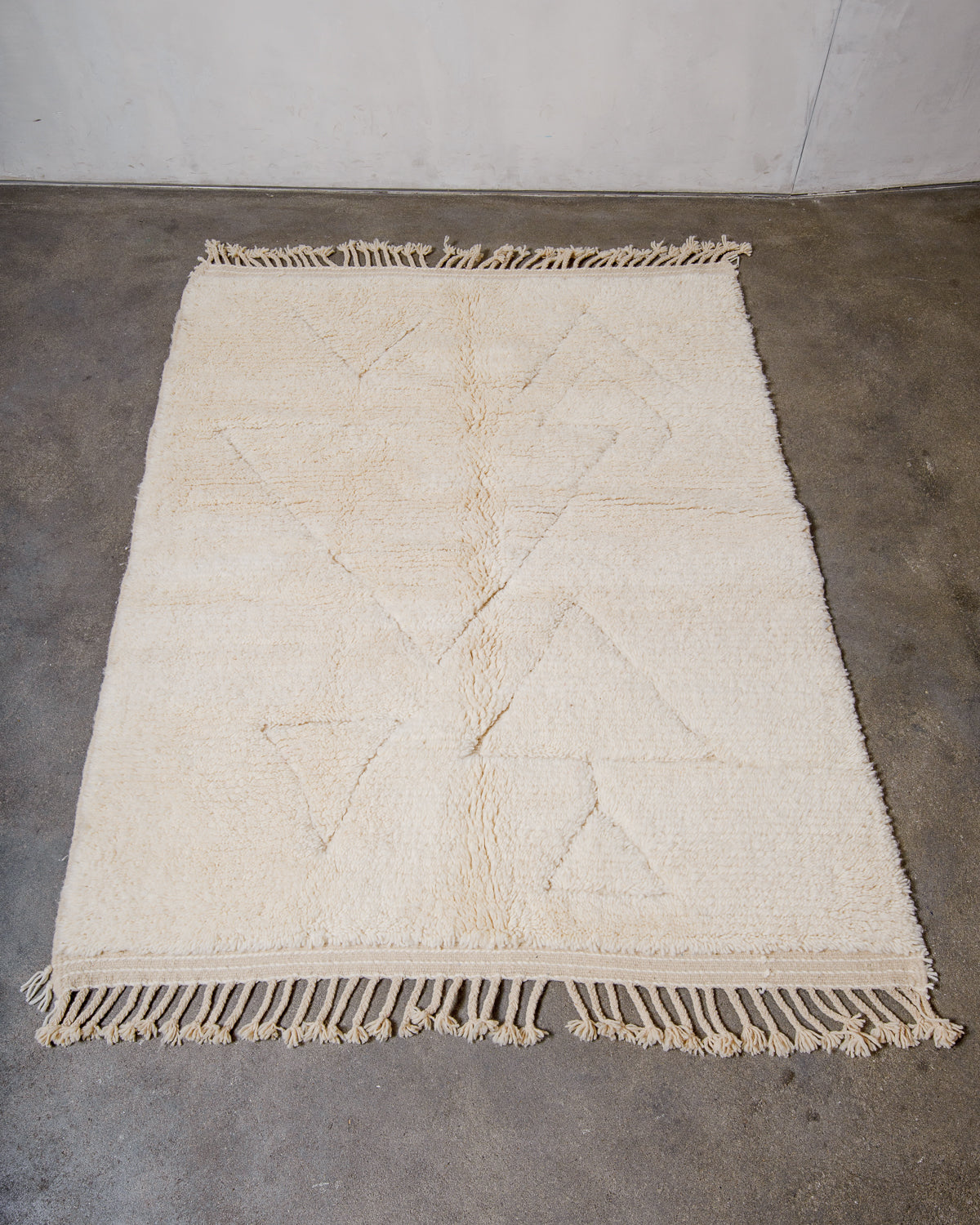 Cream wool rug with design woven in natural wool laying flat on concrete floor.